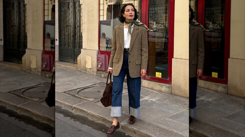 A woman in a brown blazer, jeans and a silk scarf around her neck