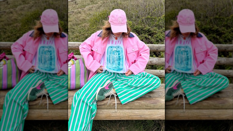 A woman sitting on a park bench in a pink jacket and pink and green striped pants