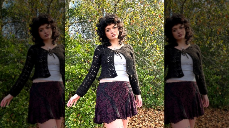 A woman standing outdoors in a mini skirt and wearing an open-weave black cardigan