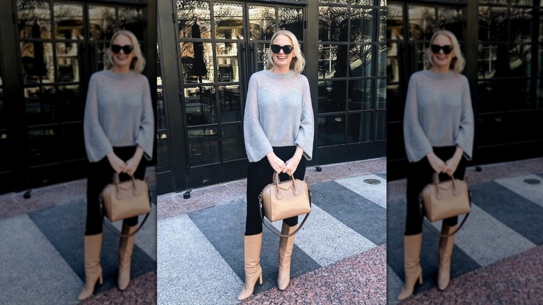 A woman standing on the street in a sheer gray sweater and wearing knee-high boots