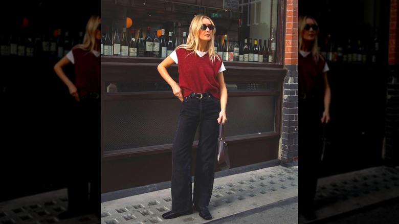 A woman standing on the street in black greens and a red sweater vest