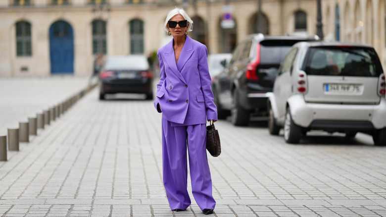 An older woman standing on the street in a purple suit