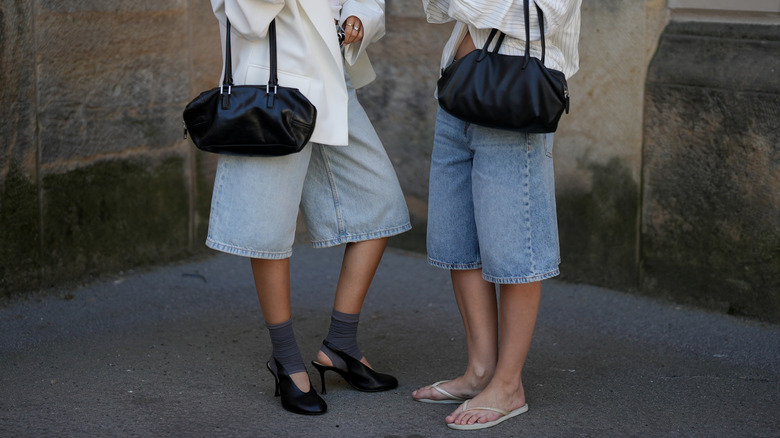 Bottom half of two people wearing large denim shorts and mules and flip flops