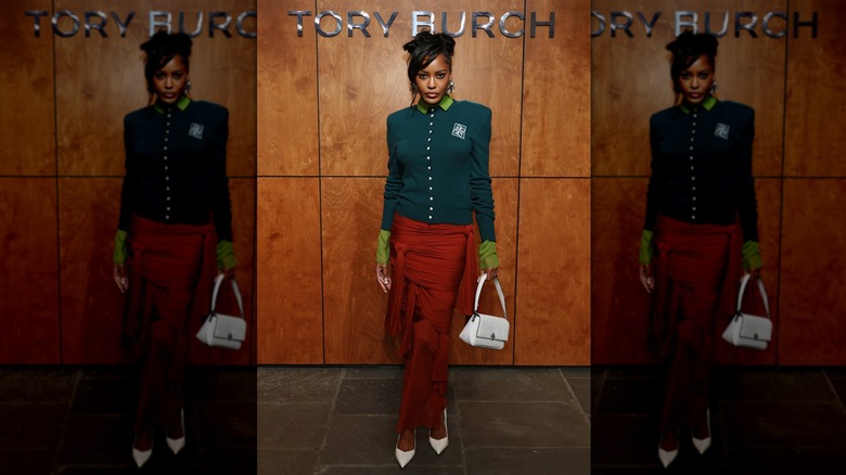 Ciara Miller poses in a green cardigan and red skirt