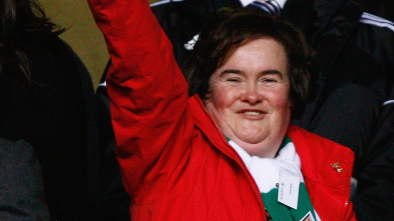 Susan Boyle smiling and waving while wearing a red coat in 2009