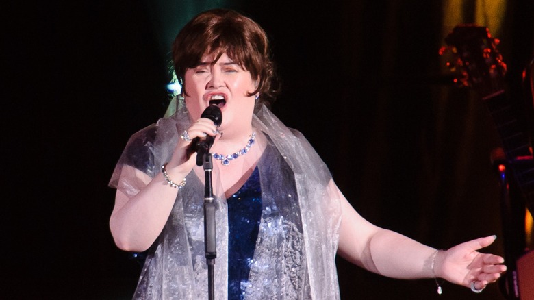 Susan Boyle performing on stage in 2014 in a blue dress and sheer wrap