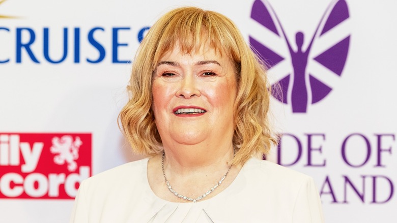 Susan Boyle smiling on the red carpet in front of a white background
