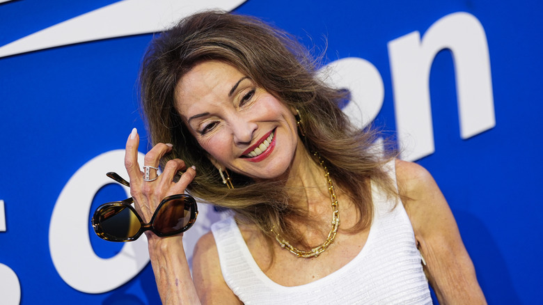 Susan Lucci in a white dress and holding sunglasses on the red carpet