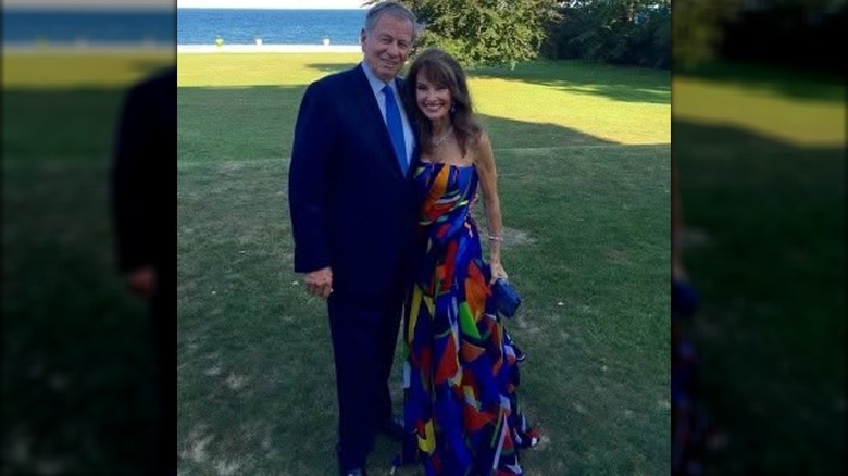 Helmut Huber and Susan Lucci posing together at their son's wedding in front of grass and the ocean
