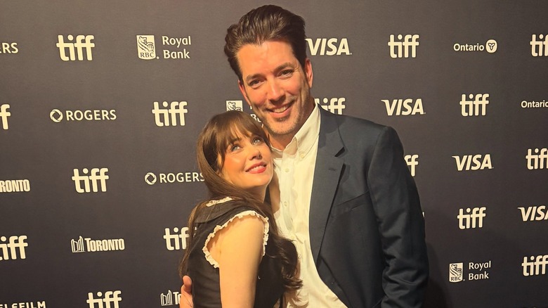 Jonathan Scott hugs Zooey Deschanel on the TIFF red carpet while she playfully looks up in a black dress