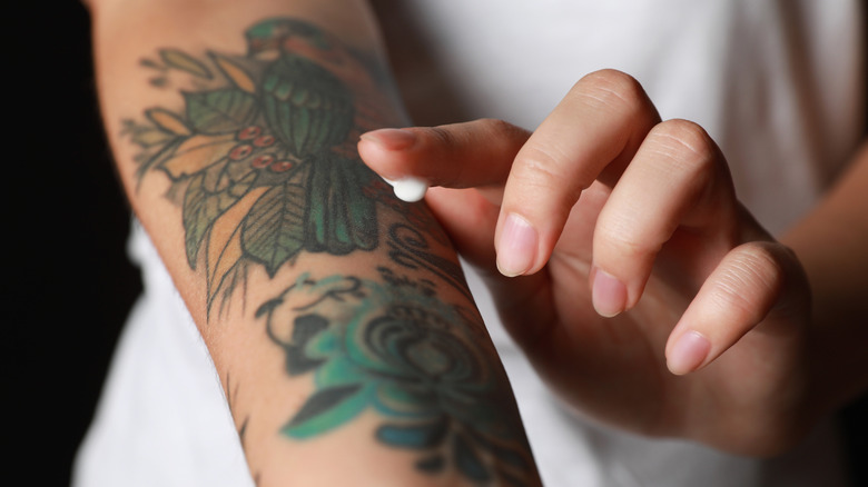 A woman puts a small dollop of cream on a new arm                          tattoo