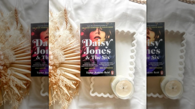 A copy of "Daisy Jones & the Six" laying on a white tray, next to a candle and some fried foliage