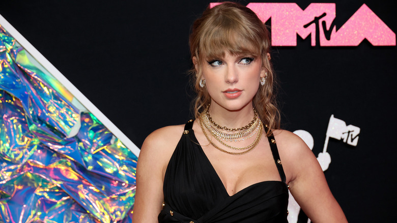 Taylor Swift looking to the side while wearing a black dress and layered necklaces at the 2023 MTV VMAs