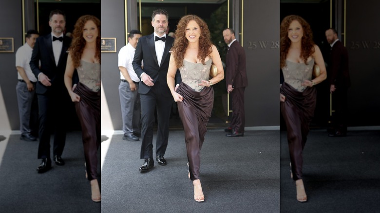 Abigail Anderson walking out of a hotel wearing a brown and gray gown with a corset bodice