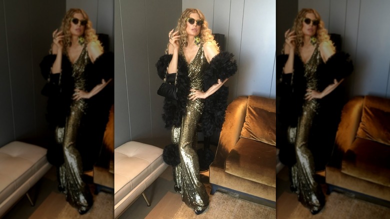 Fergie standing in a corner wearing a gold gown with a black fuzzy wrap