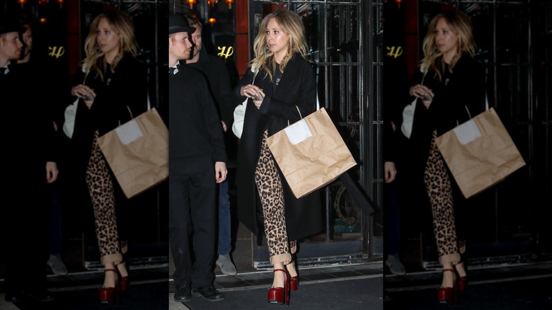 Juno Temple in leopard print pants and a black coat with red shoes