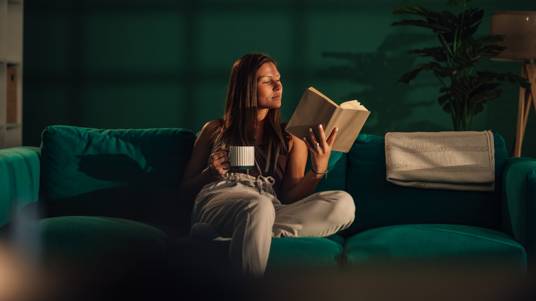 A woman reading a book on a green couch in a dim room