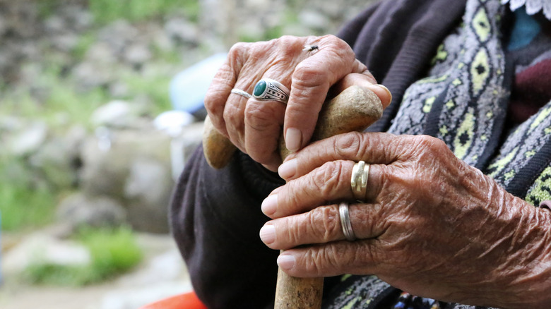Woman's hands outside wearing rings holding a cane