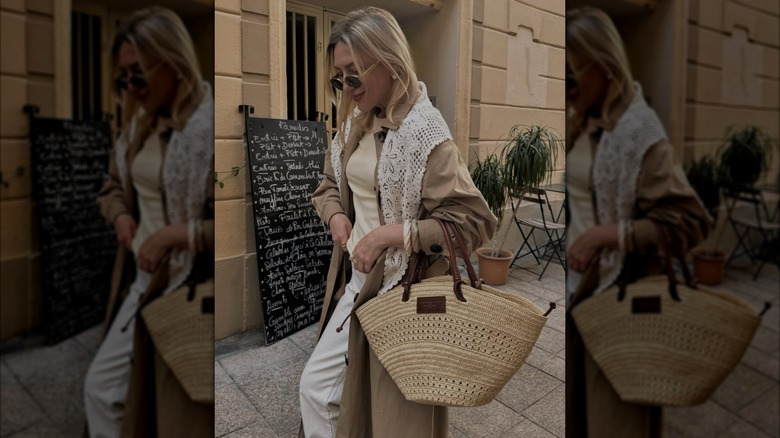 A woman carrying a raffia bag with a crochet scarf and trench coat