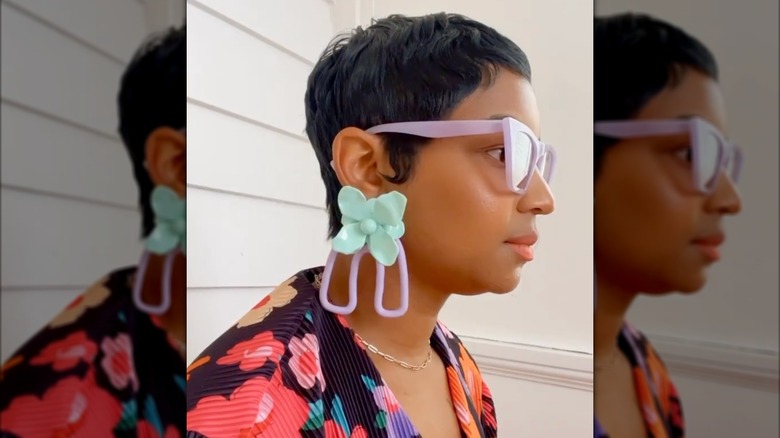 A woman wearing big blue and purple earrings with purple glasses and a bright shirt