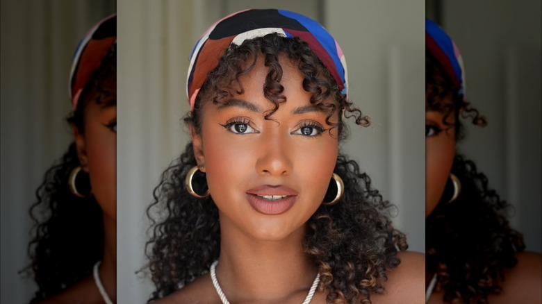 A woman wearing a silk scarf around her hair with gold hoops and a necklace