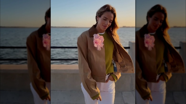 A woman wearing a brown coat and white pants with a pink flower pin