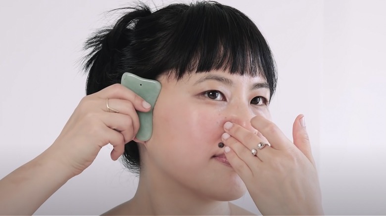 woman applying gua sha over face mask