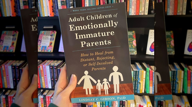 A hand holding up "Adult Children of Emotionally Immature Parents" in front of a bookcase