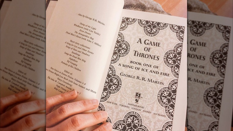 A hand holding open a copy of "Game of Thrones" to the title page