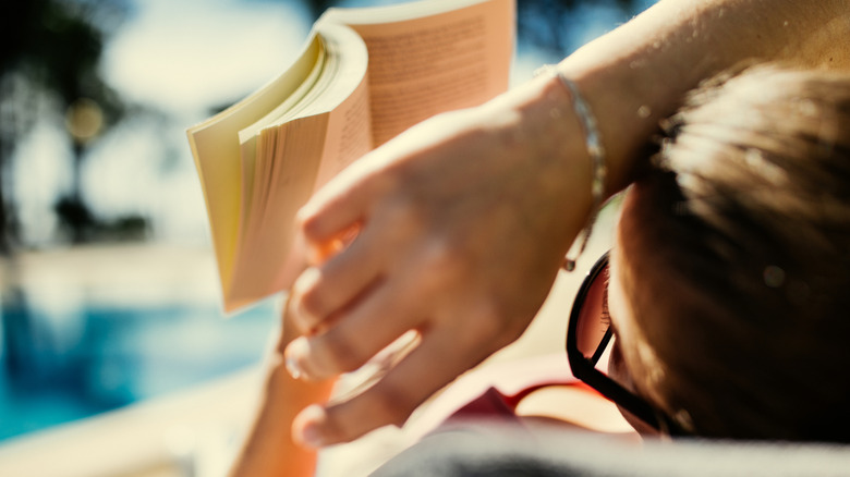 A woman sits by the pool and reads a book