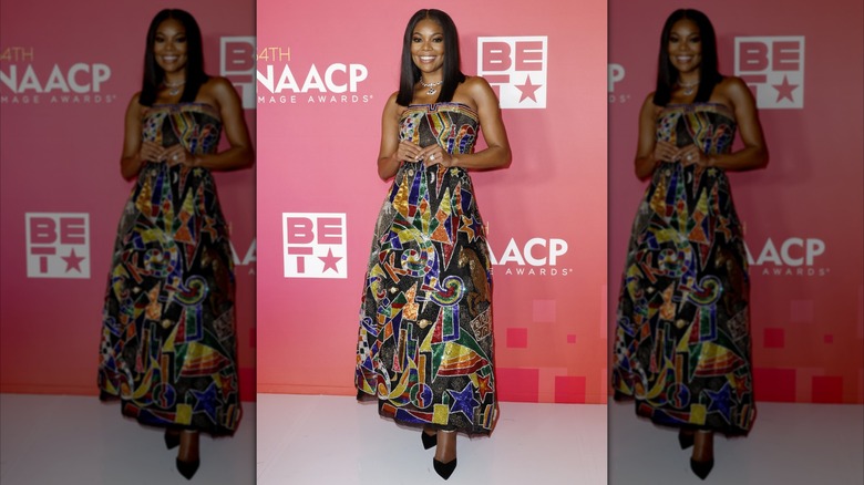 Gabrielle Union posing at the NAACP Image Awards while wearing a colorful, ankle-length dress from Versace