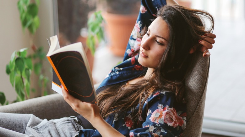 A brunette woman sitting in a chair while reading a book