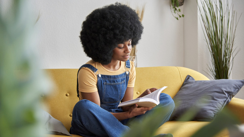 A woman sits on a sofa and reads a book