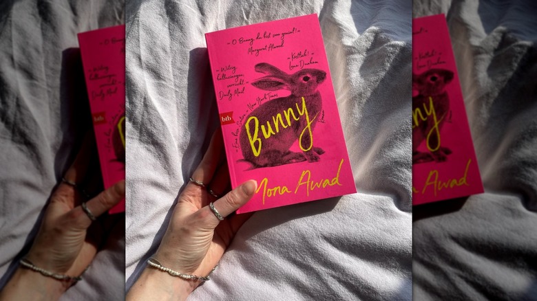 A hand holding the novel "Bunny" with a white sheet in the background