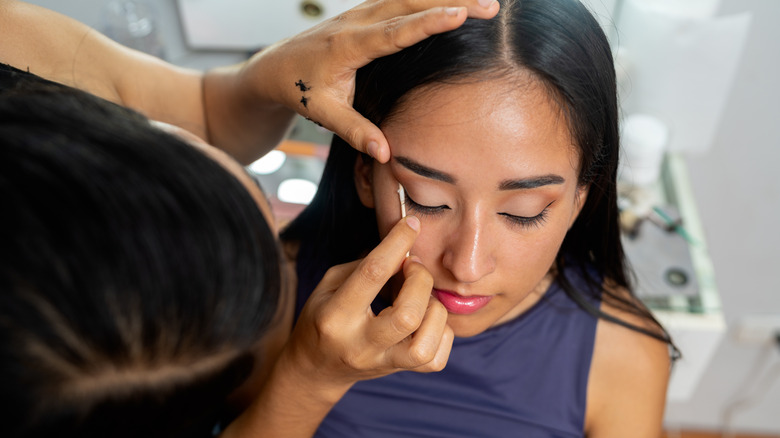 Makeup artist applying eyeliner to a young woman's eye with a cotton swab
