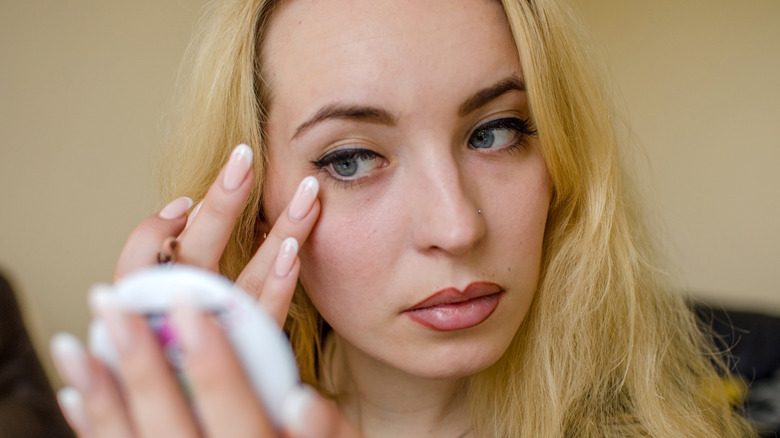 Close-up of woman with blue eyes looking into compact mirror while swiping her fingers near her winged eyeliner