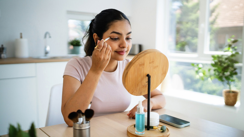 Women applying eyeliner in front of small mirror