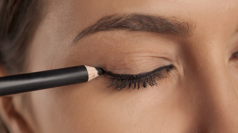 Women applying a black kohl eyeliner to top lid