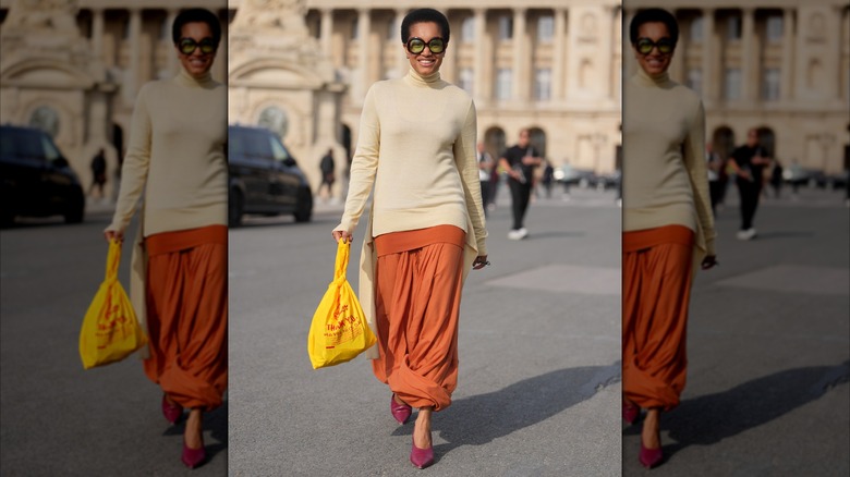 A woman walking the streets and smiling in a burnt orange skirt and beige sweater