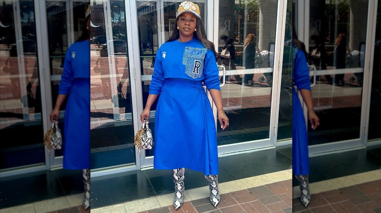 A woman wearing a cap with a cropped cobalt blue sweatshirt and skirt