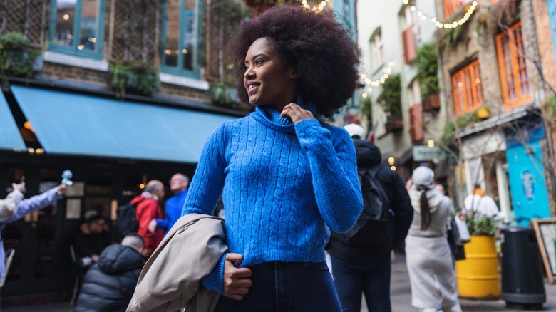A woman standing in the middle of a town in a blue sweater while holding a coat
