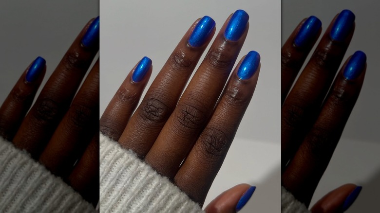 Open hand showing bright blue nails with a slight sheen against a grey background