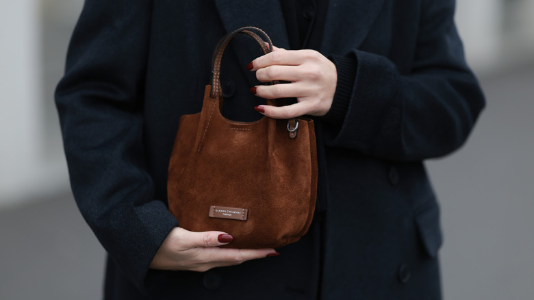 A woman with burgundy nails holding a small handbag