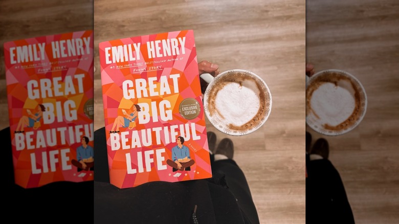 A person looking down and holding a copy of Great Big Beautiful Life and a cup of coffee