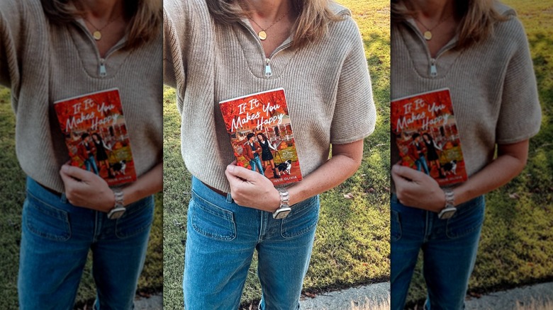 A woman holding a copy of If It Makes You Happy and wearing a sweater and jeans