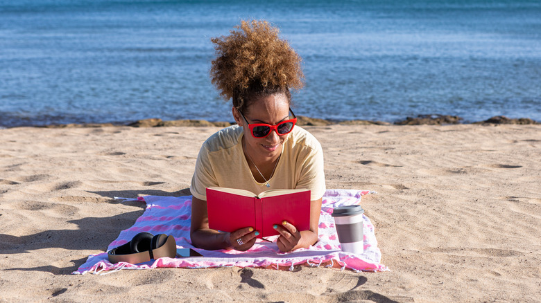 A woman lies on the beach and reads a book