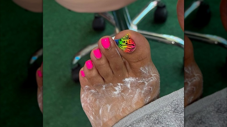 A close up of a woman getting a pedicure with pink and bright toe nails