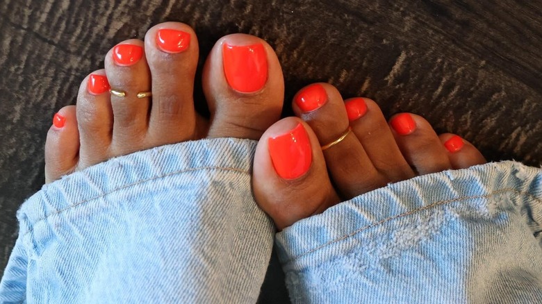 A woman with a red orange pedicure wearing blue jeans