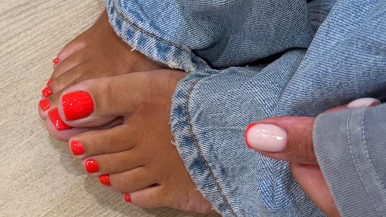 A woman wearing blue denim jeans with an orange red pedicure