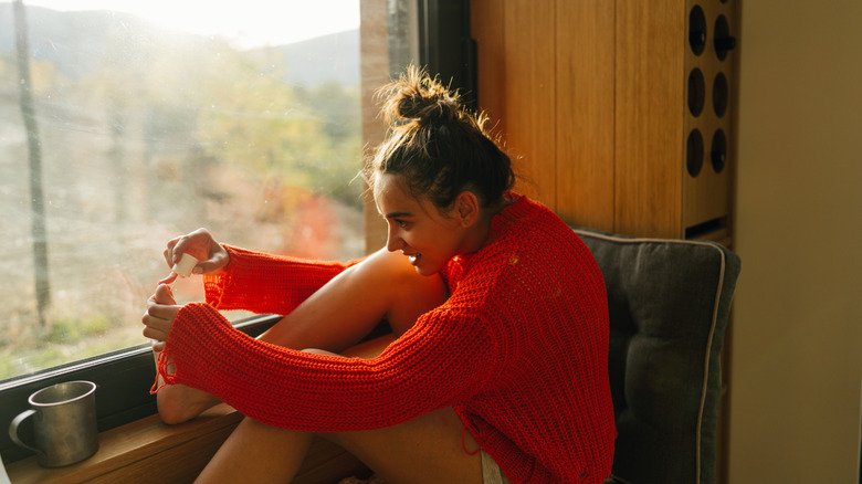 women in orange jumper sat sofa in robe painting toenails